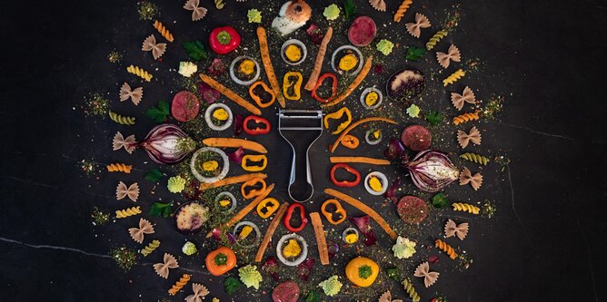 Photo of a vegetable peeler. All around are pieces of vegetables and pasta. | © SONNENTOR