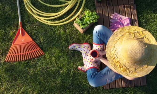 Düngen mit Teeresten | © SONNENTOR Auf dem Foto ist eine Frau zu sehen die mit einer Tasse Tee im Garten sitzt. Daneben sind ein Gartenschlauch, ein Rechen und Salatpflanzen zu sehen. | © SONNENTOR