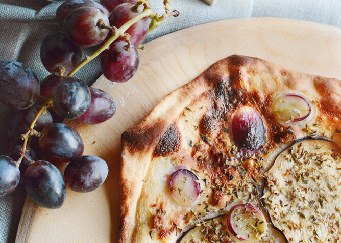 Trauben Focaccia | © SONNENTOR Auf dem Foto sieht man Focaccia mit roten Trauben darauf. Darüber sind verschiedene Kräuter gestreut. | © SONNENTOR